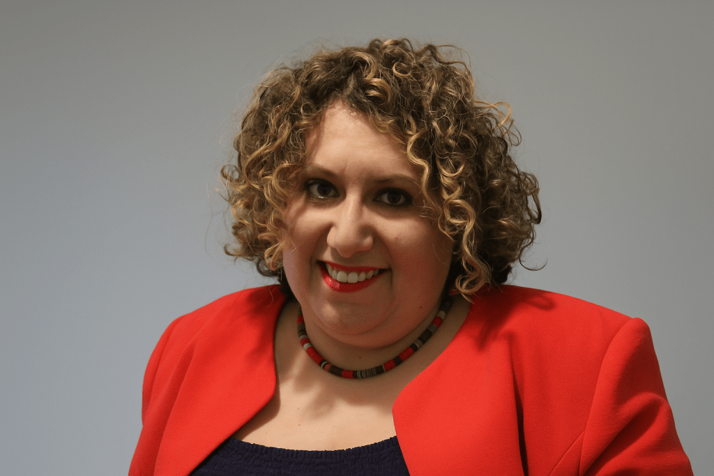 Image of Pamela Welsh, curly haired woman wearing a prink jacket